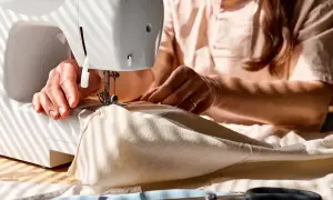 Ręce kobiety szyją na maszynie. Powstaje delikatna tkanina, może to będzie woal na sukienkę?