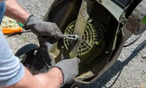 Ręce w rękawiczkach odkręcają nóż kosiarki, przygotowując ją do przeróbki na aerator.