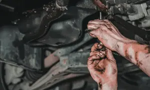 Brudne ręce mechanika pracującego pod samochodem, zastanawiającego się, jaki smar do przegubów będzie najlepszy.