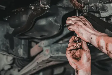 Brudne ręce mechanika pracującego pod samochodem, zastanawiającego się, jaki smar do przegubów będzie najlepszy.