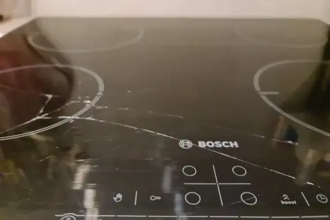 Pęknięta płyta indukcyjna Bosch z widocznymi zarysowaniami i pęknięciami na szkle.