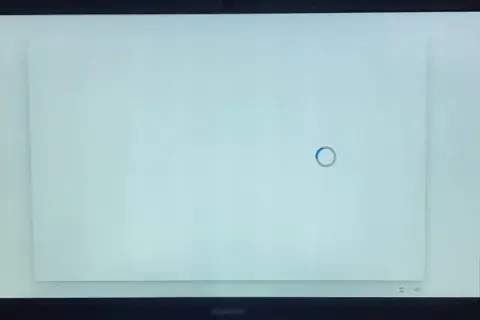 Jasny, biały ekran laptopa z niebieskim kółkiem ładowania pośrodku. Czekam na zakończenie procesu.