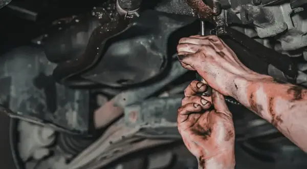 Brudne ręce mechanika pracującego pod samochodem, zastanawiającego się, jaki smar do przegubów będzie najlepszy.