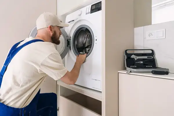 Serwisant sprawdza, czy nie ma urwanego bębna w pralce. Obok leży walizka z narzędziami.