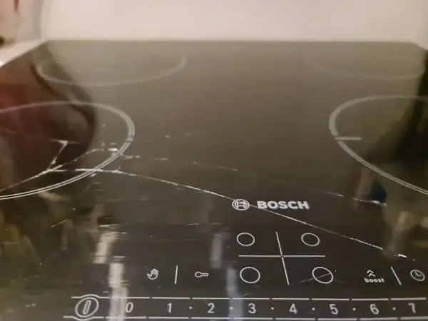 Pęknięta płyta indukcyjna Bosch z widocznymi zarysowaniami i pęknięciami na szkle.