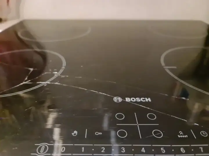 Pęknięta płyta indukcyjna Bosch z widocznymi zarysowaniami i pęknięciami na szkle.